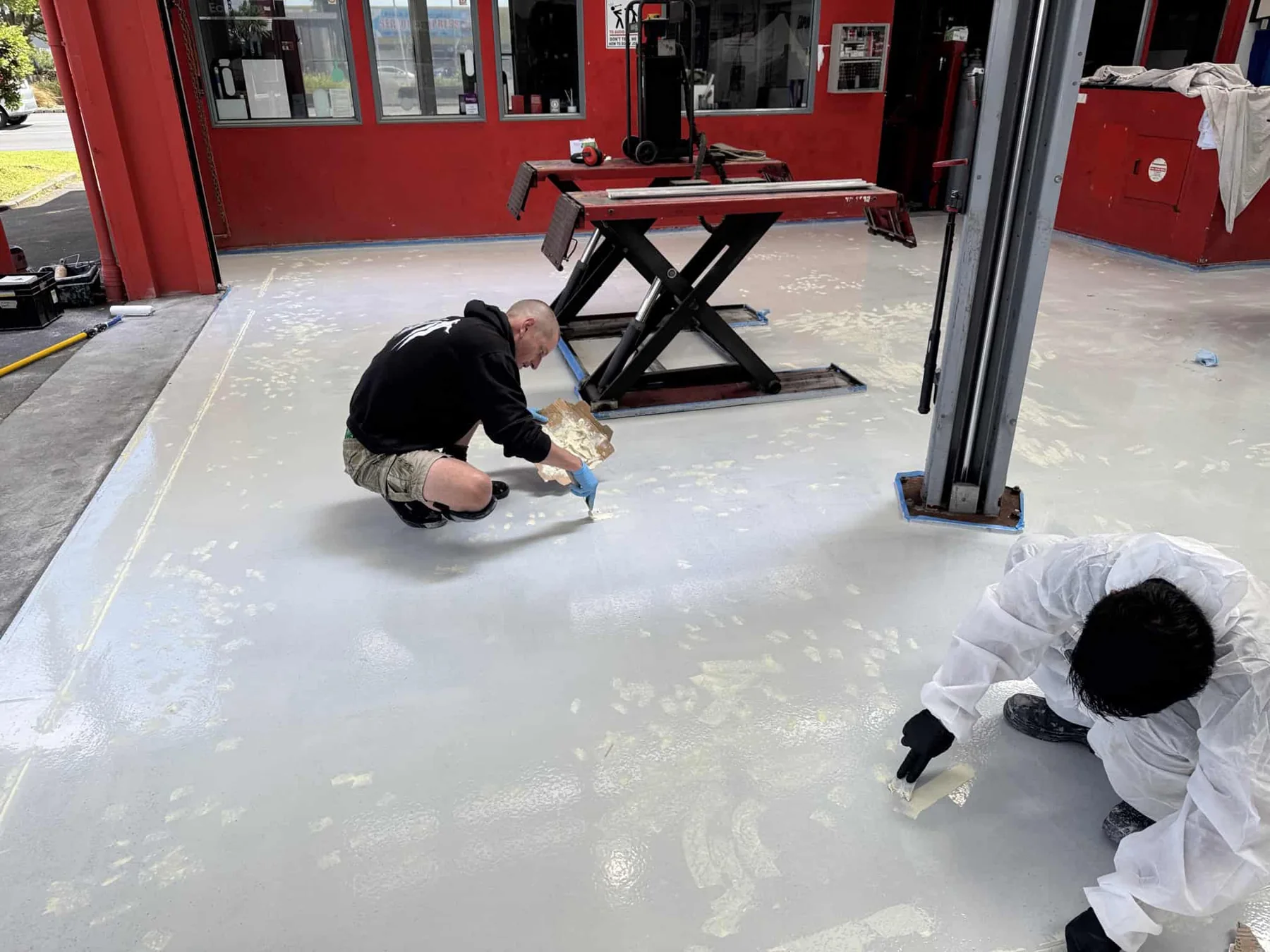Contractors repairing and coating a prepared concrete workshop floor