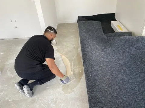 Installer applying adhesive while fitting charcoal garage carpet over concrete