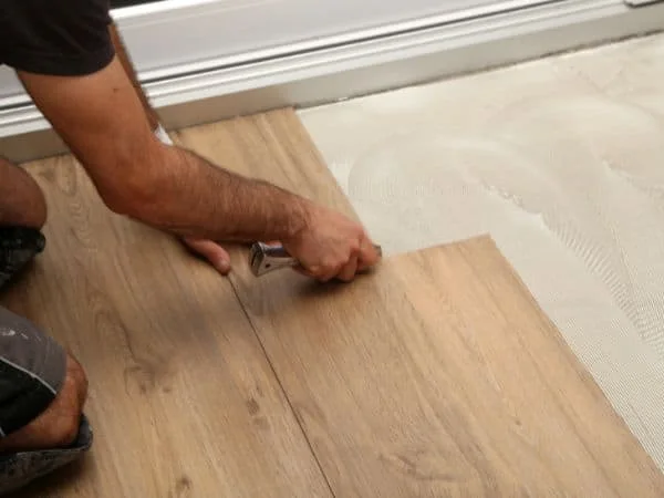 Installer trimming wood-look residential vinyl flooring beside a wall